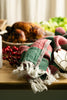 Fringed holly tea towel draped on a table with roasted poultry and seasonal decor