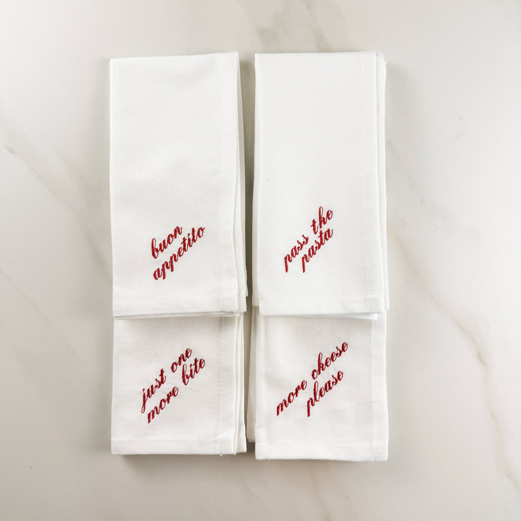 Four white napkins with different red embroidered Italian sayings