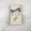 Set of four natural linen napkins tied with striped ribbon, embroidered with “Eat your vegetables”