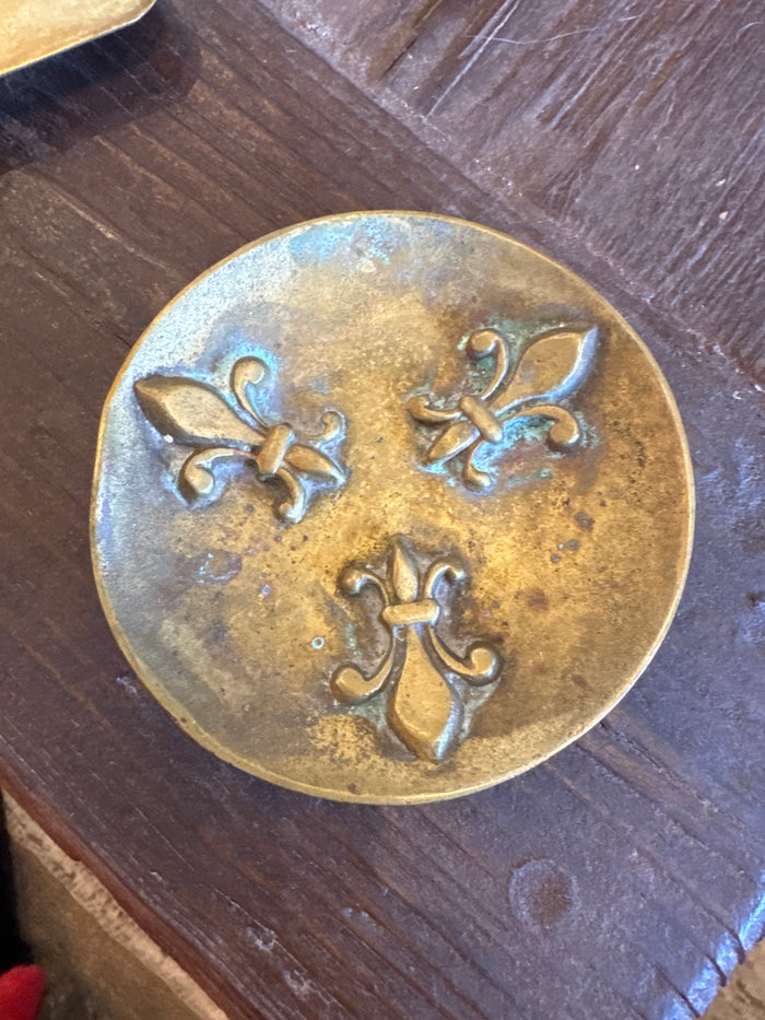 Antique brass ashtray with circular fleur de lis emblem on the lid