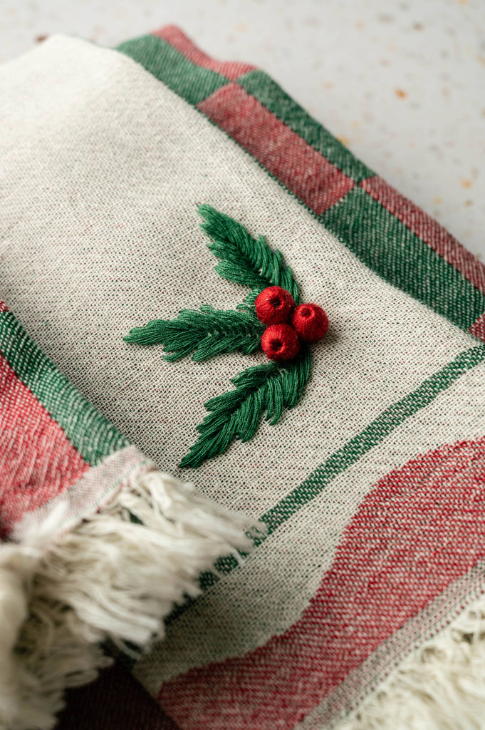 Cream tea towel with holly berry embroidery, green/red striped border, and white fringe