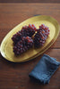 Brass oval tray (M) with clusters of red grapes, on wood surface