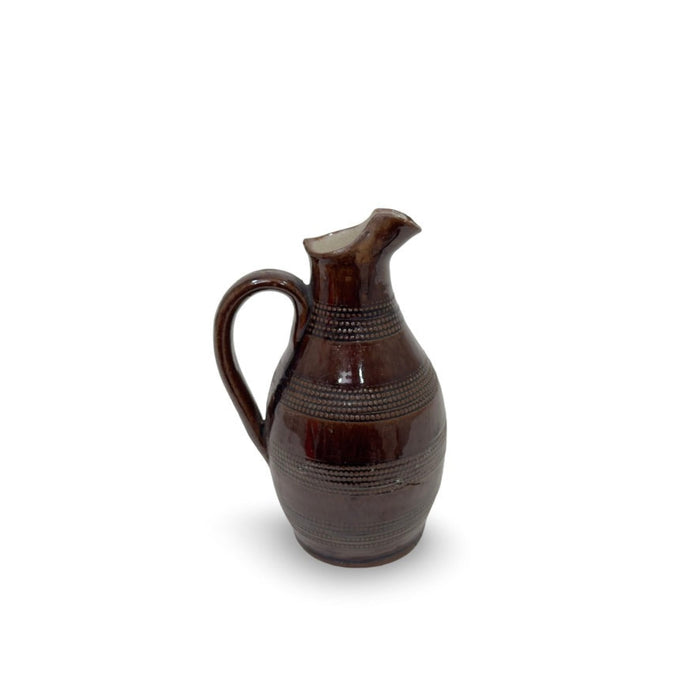 Antique stoneware pitcher in dark brown with handle and spout, patterned bands.
