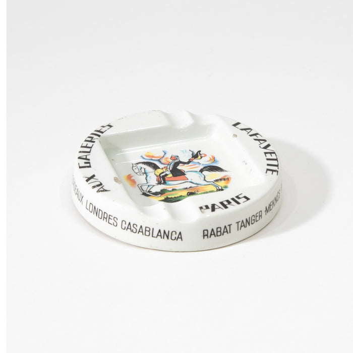 White ceramic round ashtray with colorful central print and gold-toned rim text