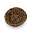 A round, hand-woven basket made of natural brown and tan fibers, photographed from a top-down angle on a white background with a soft drop shadow.