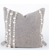 Gray pillow with white pom-pom trim on a white background