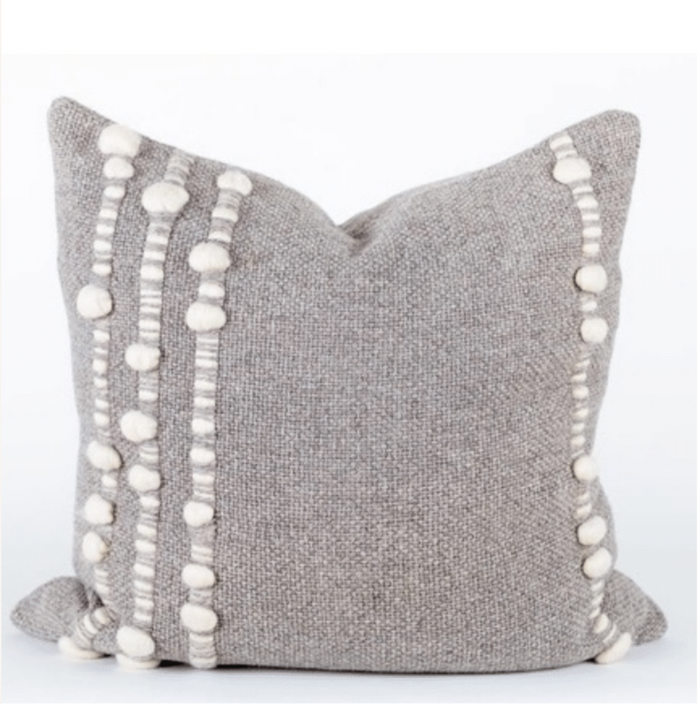 Gray pillow with white pom-pom trim on a white background