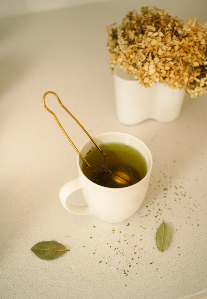 Gold stainless steel tea strainer resting in a cup of tea with mesh ball and loop handle