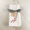 Folded white dinner napkins with red embroidered Italian saying, tied with striped ribbon