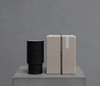 Black cylindrical scented candle with lid, beside beige gift box with dark ribbon