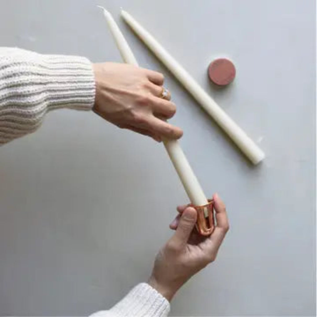 Copper-tone candle sharpener tapering white taper candles with hands.