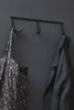 Wall-mounted iron triple hook rack with three curved hooks holding garments