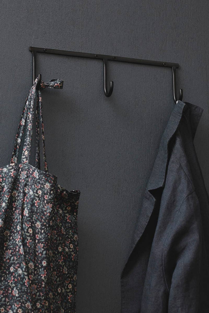 Wall-mounted iron triple hook rack with three curved hooks holding garments